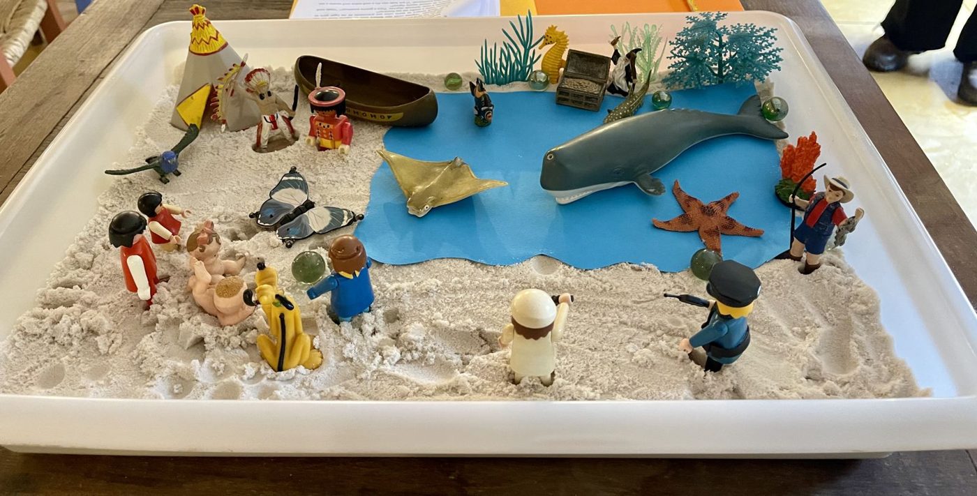 Caixa de areia com lago azul, miniaturas de animais marinhos e bonecos