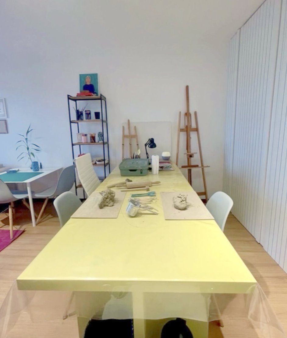 Sala do consultório com mesa ampla, cavaletes de pintura e argila sobre a mesa